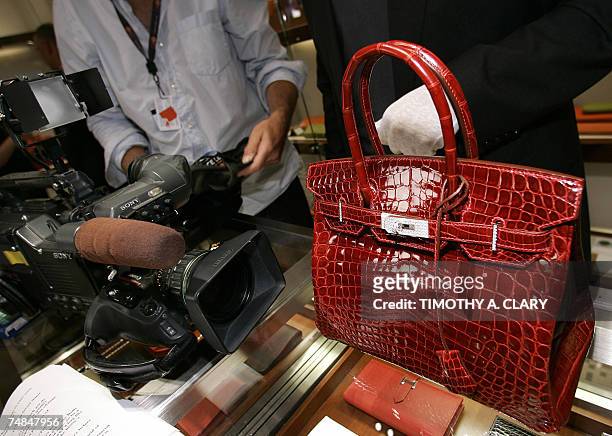 New York, UNITED STATES: A employee holds displays a 129,000 USD crocodile Hermes Birkin Bag for the press during a private opening for the new...