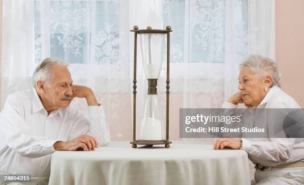senior couple staring at hourglass - eenheid stockfoto's en -beelden