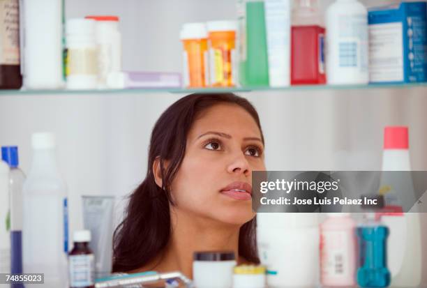 hispanic woman looking in medicine cabinet - bathroom cabinet stock pictures, royalty-free photos & images