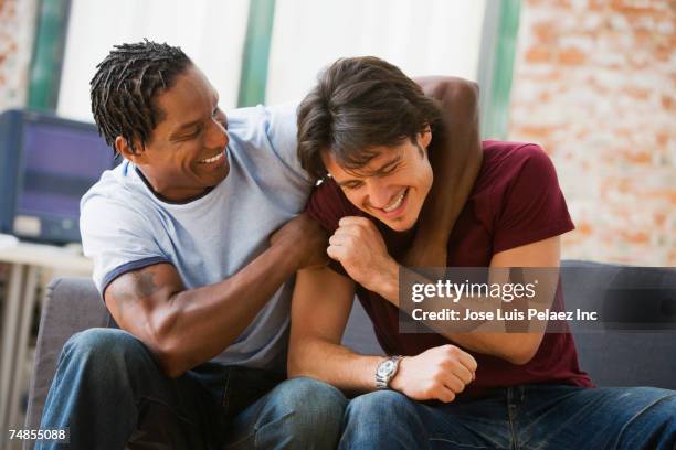 multi-ethnic men hugging on sofa - man cave stock pictures, royalty-free photos & images