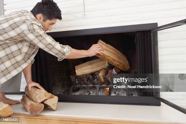 asian man putting logs in fireplace - brandhout stockfoto's en -beelden