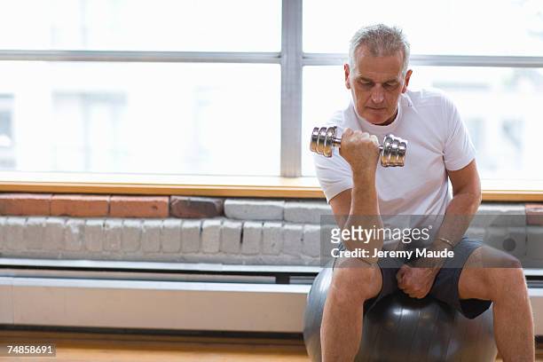 senior man sitting on fitness ball doing exercise - musculation des biceps photos et images de collection