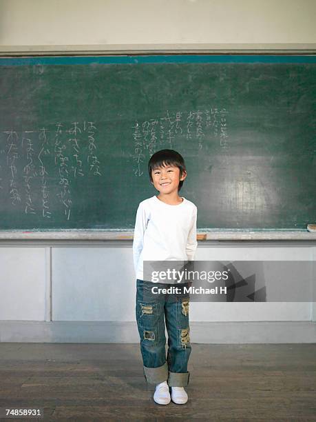boy (5-7) standing by blackboard in classroom, portrait - classroom-front-view stock-fotos und bilder