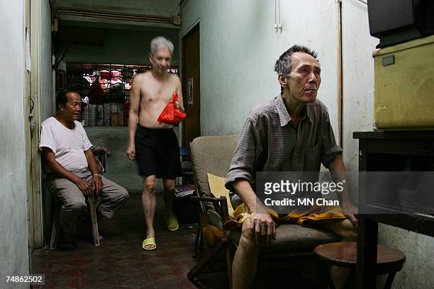 Men sit in corridor outside their cage homes on June 20, 2007 in Hong Kong, China. The poorest of Hong Kong's citizens live in cage homes, steel mesh...