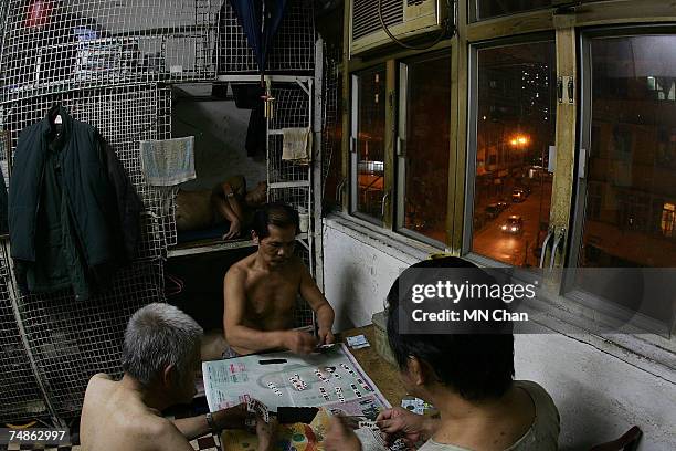 Men play cards beside cage dwellings on June 20, 2007 in Hong Kong, China. The poorest of Hong Kong's citizens live in cage homes, steel mesh box...