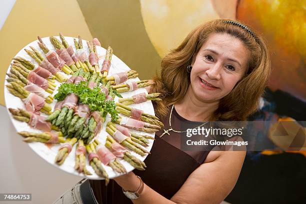 portrait of a mature woman showing prosciutto wrapped asparagus arranged in a plate - prosciutto wrapped stock pictures, royalty-free photos & images