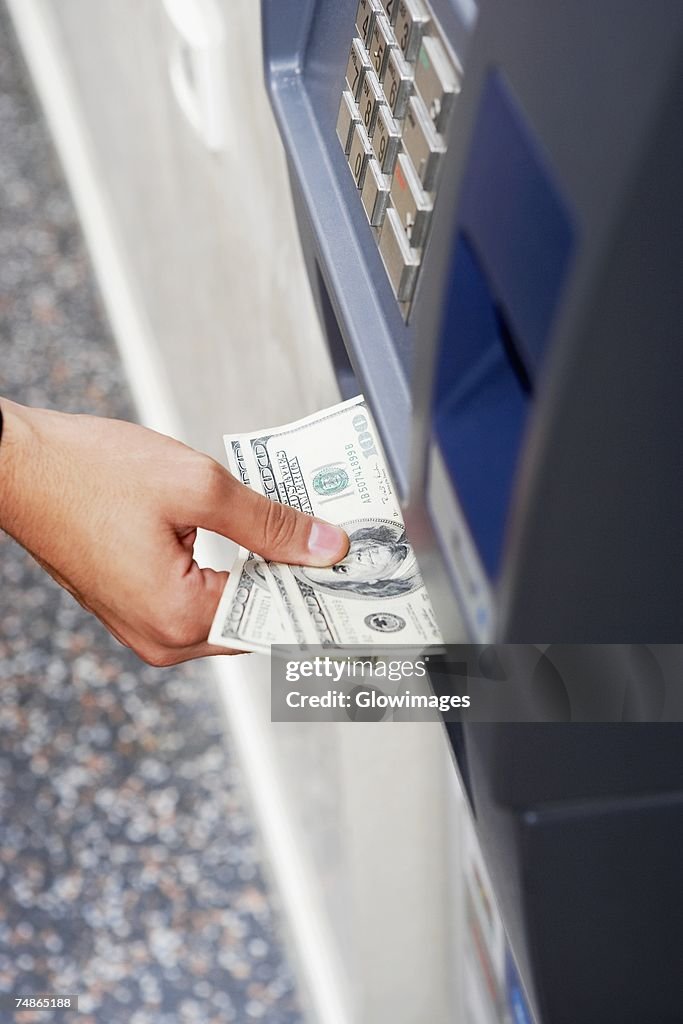 Close-up of a person's hand receiving one hundred dollar bills from an ATM