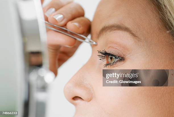 close-up of a mid adult woman tweezing her eyebrows - eyebrow tweezers stock pictures, royalty-free photos & images