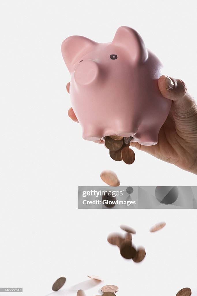 Close-up of a person dropping coins from a piggy bank