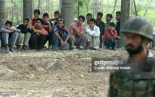 An Indian Army soldier stands guard as Kashmiri Muslim youths are detained for questioning after an explosion on the outskirts of Srinagar, 24 June...