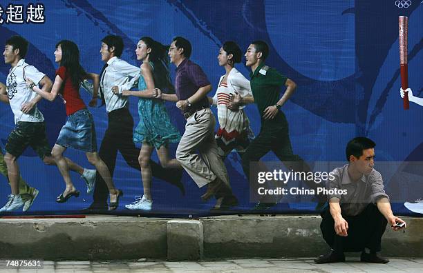 Man sits in front of a billboard during a ceremony to launch the Olympics torchbearer selection program sponsored by Lenovo Group June 24, 2007 in...