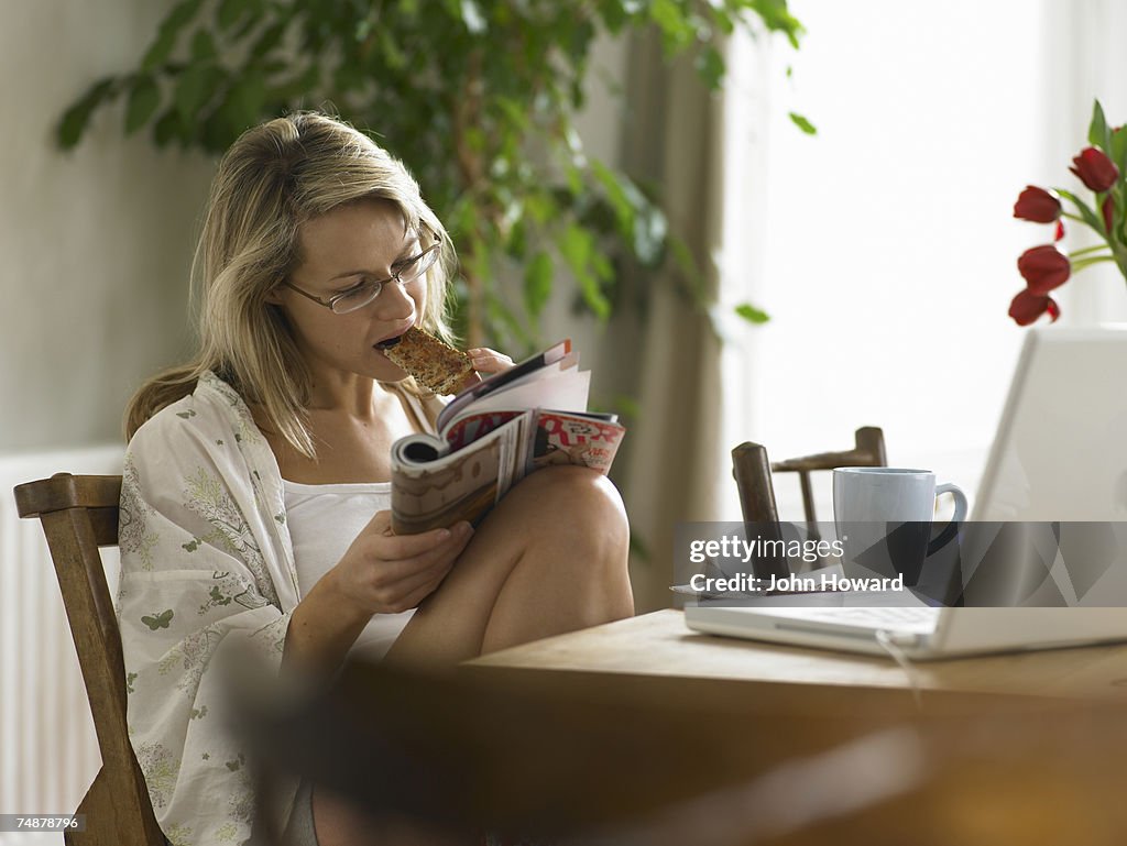 Young woman having breakfast while reading magazine