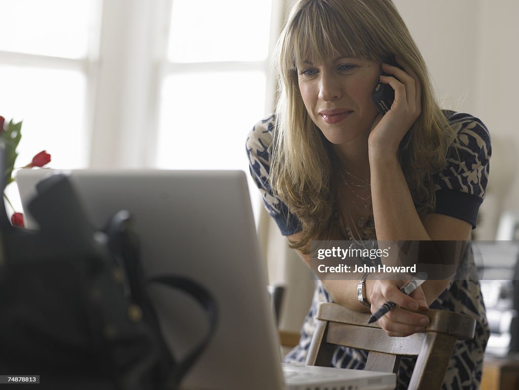 Young woman looking at laptop while using cell phone, smiling