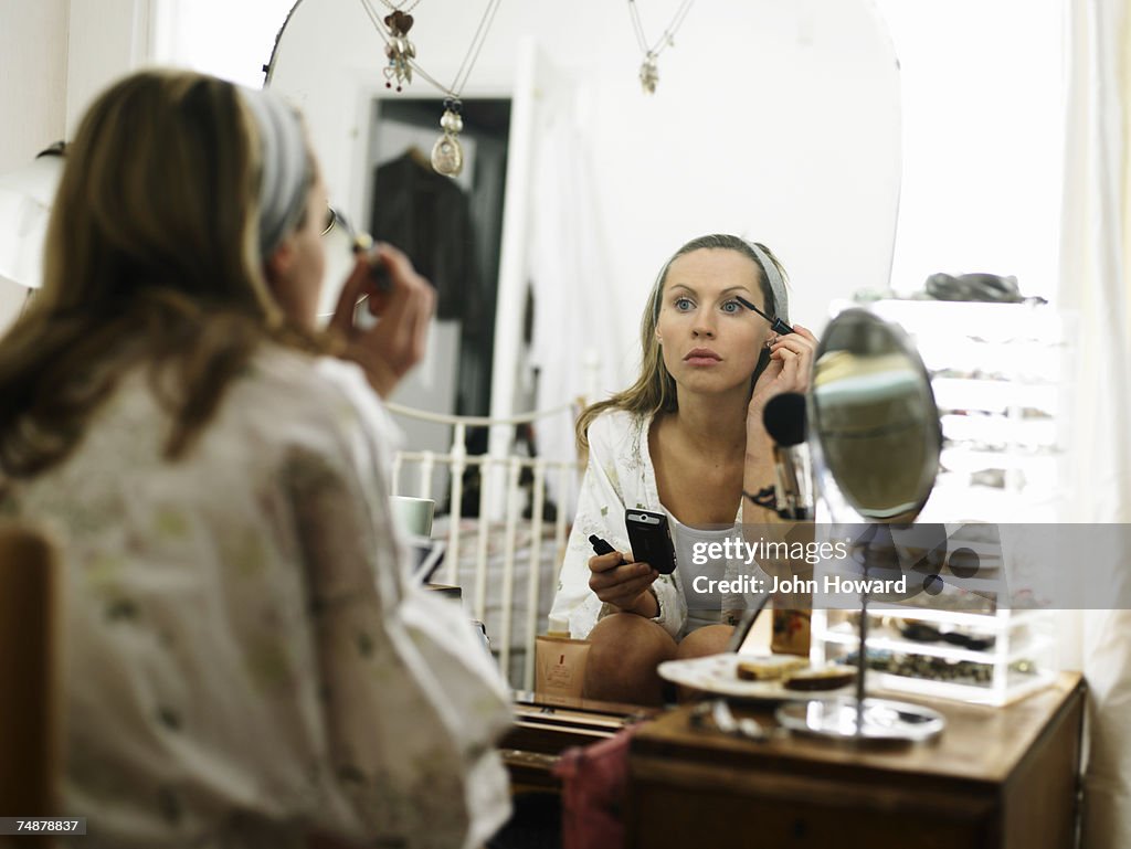 Young woman sitting at dressing table applying make-up