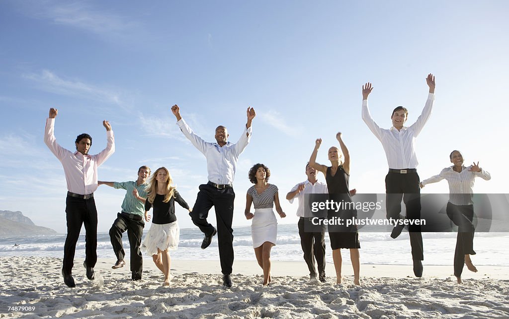 Nine businessmen and women jumping on beach, smiling