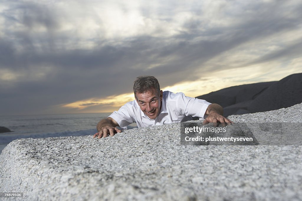 Man clinging onto rock on beach