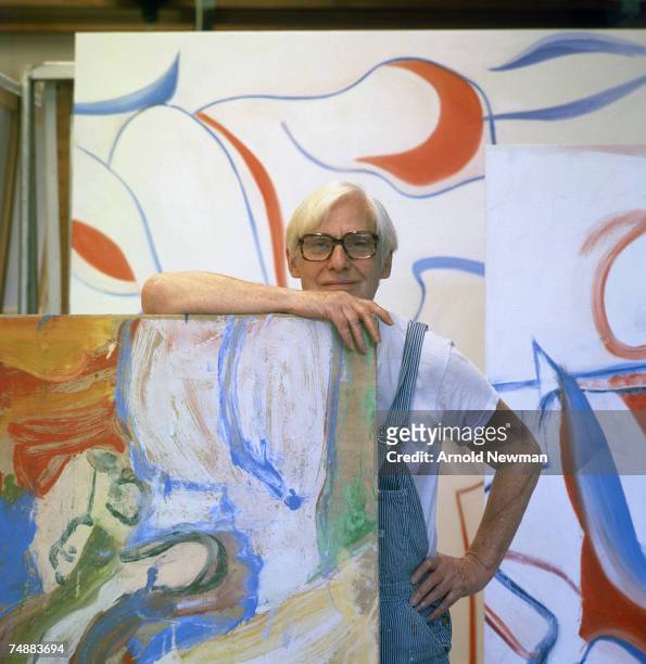 Portrait of Dutch-born American artist Willem de Kooning as he poses in his studio, dressed in blue and white striped overalls, Springs, Long Island,...