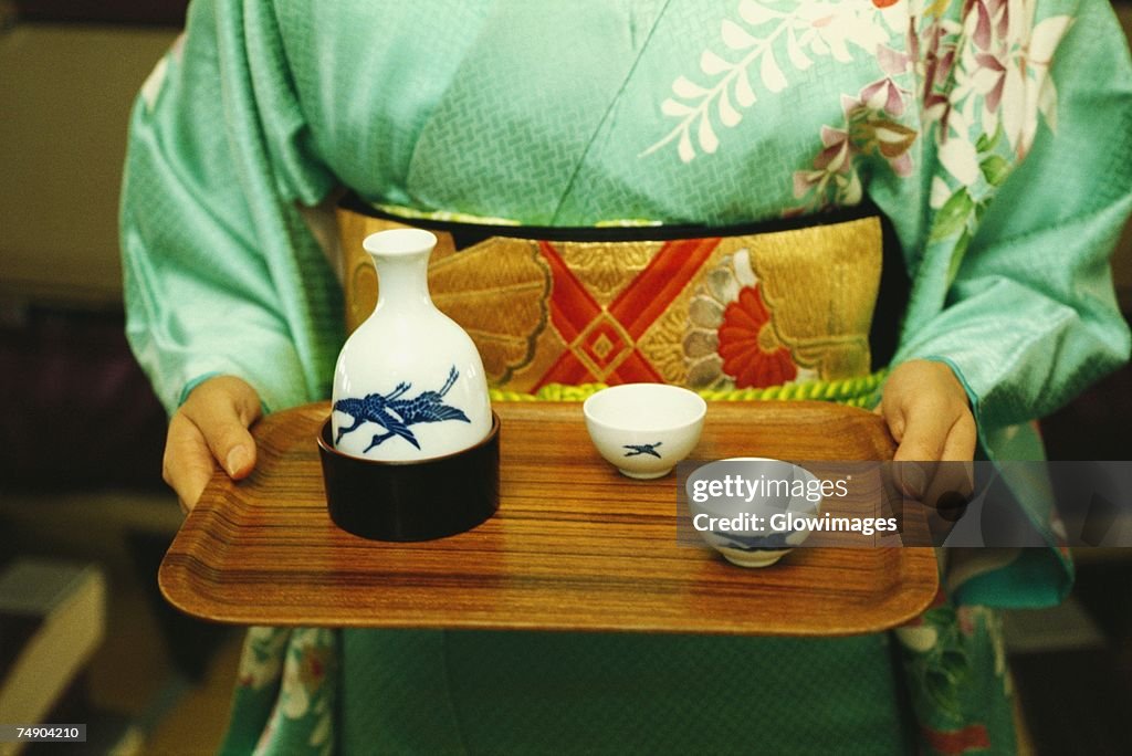 Mid section view of a woman holding saki on tray, Japan