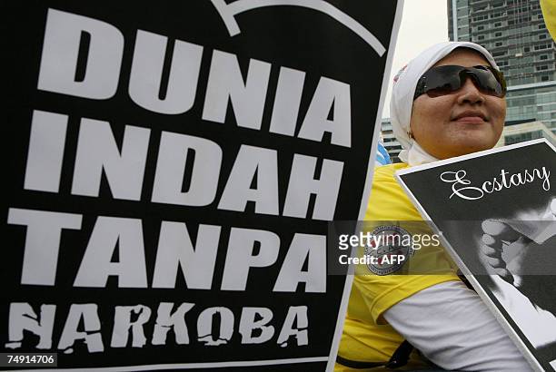 An Indonesian woman sits next to an anti anti-drugs poster that read "World is Beautiful Without Drugs", during a campaign to mark the United Nations...