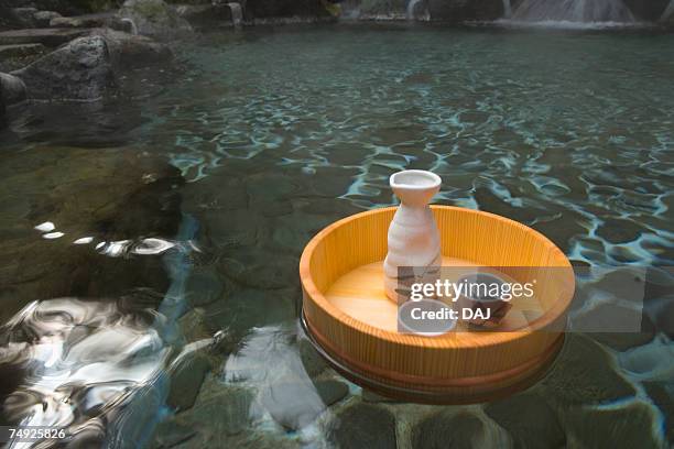 sake bottle and cups in a wooden tub floating on a japanese public bath, hot spring, high angle view, japan - saké bildbanksfoton och bilder