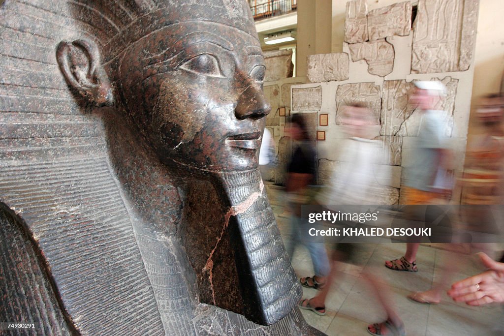 Tourists walk past a statue of Queen Hat...