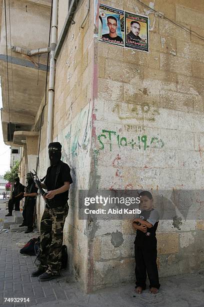 Palestinian boy stands next to masked members of the Islamic Jihad Movement while they take up position during clashes on June 27, 2007 in Gaza City,...