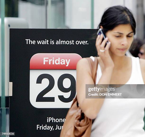 New York, UNITED STATES: A customer talks on the phone as she walk past a sign announcing the iPhone at the Apple store in New York 26 June 2007. The...