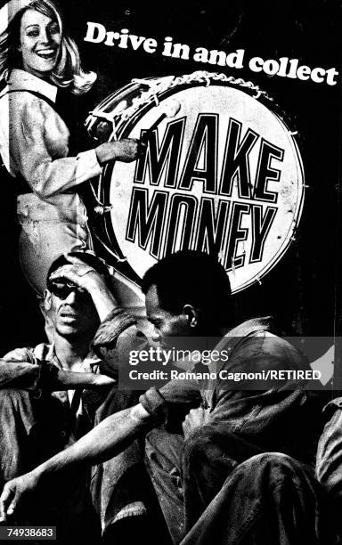 Two men in overalls sitting by an advertising poster depicting a smiling woman banging a bass drum, London, 1966.