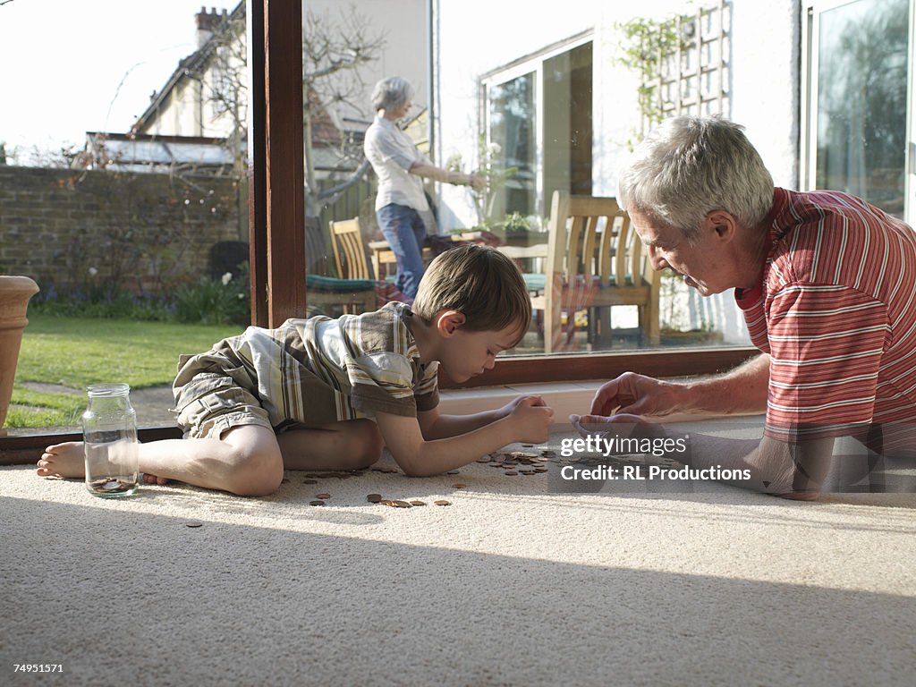 Grandfather and grandson (5-7) counting coins on floor