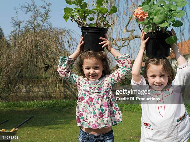 two girls (4-6) holding plants above heads, portrait - carrying pot plant stock pictures, royalty-free photos & images