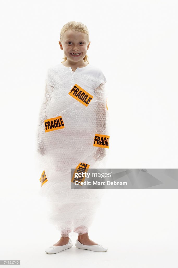 Girl (7-9) wrapped in bubble wrap labelled fragile, smiling, portrait