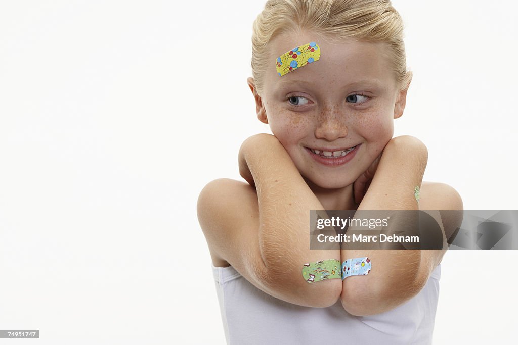 Girl (7-9) with plasters on head and arms, smiling