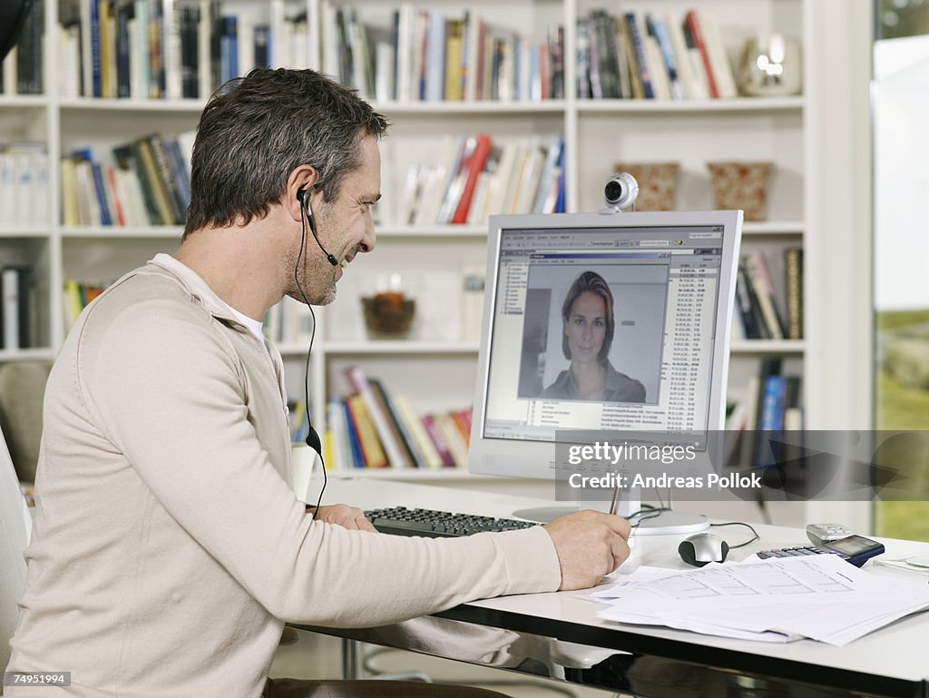 Mid Adult Man Wearing Headset Videoconferencing with Woman