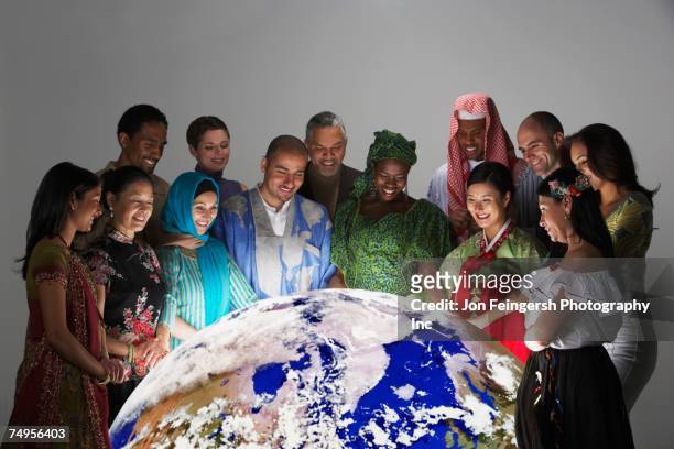 multi-ethnic people in traditional dress looking at globe - culturen stockfoto's en -beelden