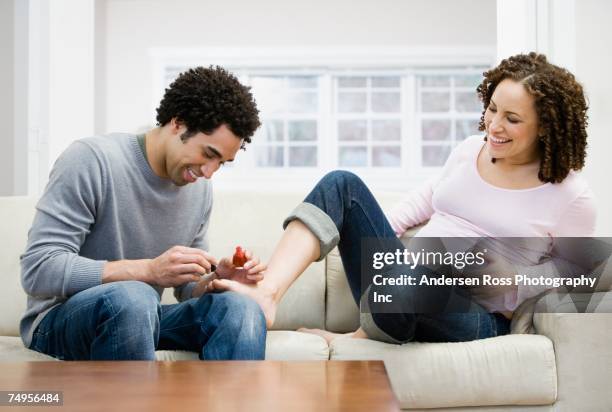 african man painting pregnant wife's toenails - laughing teen stockfoto's en -beelden