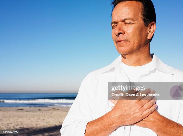 hispanic man with hands over heart at beach - hand aufs herz stock-fotos und bilder