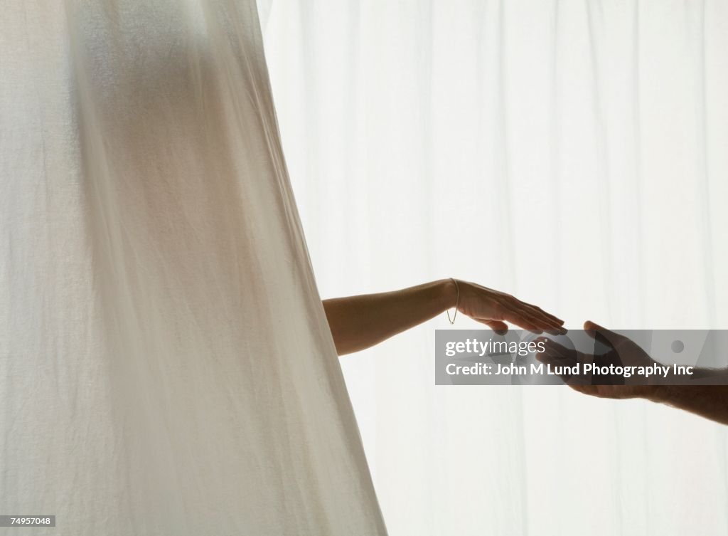 Hispanic couple reaching for each other through curtain