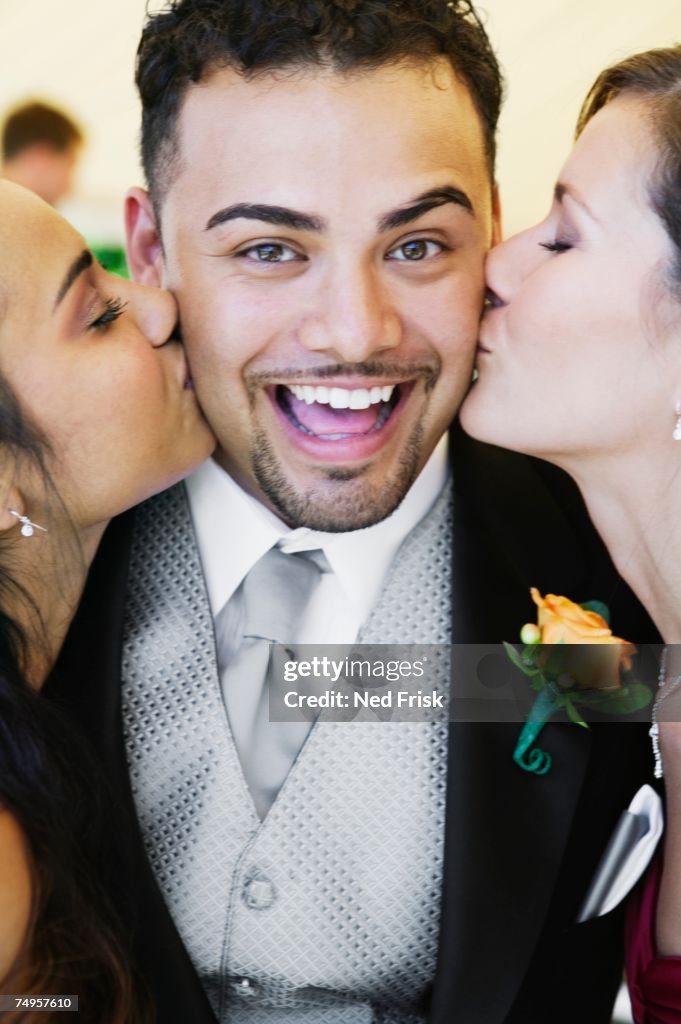 Groom being kissing by two women