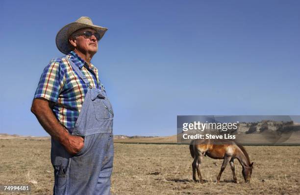Farmer Bob Roberts stands in his dry, cropless field, while a horse looks for grass to eat in the background, Scottsbluff, Nebraska, mid 2002.