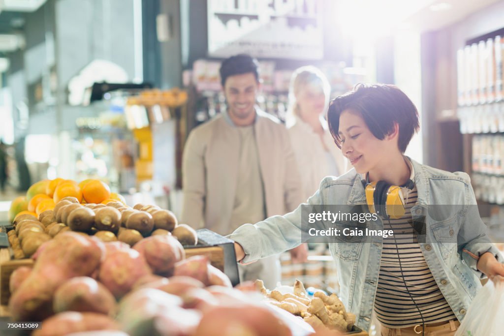 Young woman with headphones grocery shopping, browsing produce in market