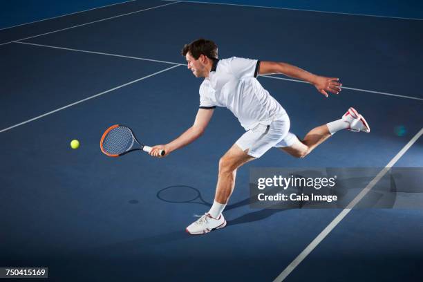 male tennis player playing tennis, reaching with tennis racket on tennis court - blue tennis racket stock pictures, royalty-free photos & images