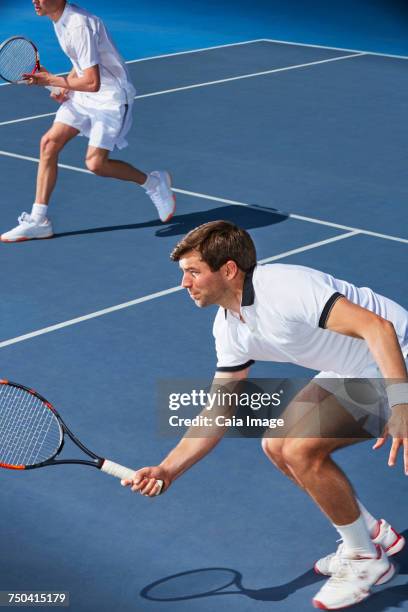 determined young male tennis doubles players poised with tennis rackets on tennis court - doubles stock pictures, royalty-free photos & images