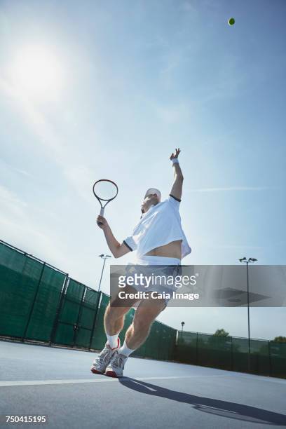 young male tennis player playing tennis, serving the ball on sunny tennis court - tennis court and low angle stock-fotos und bilder