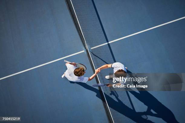 overhead view young male tennis players handshaking at net on sunny blue tennis court - tennis 2017 stock-fotos und bilder