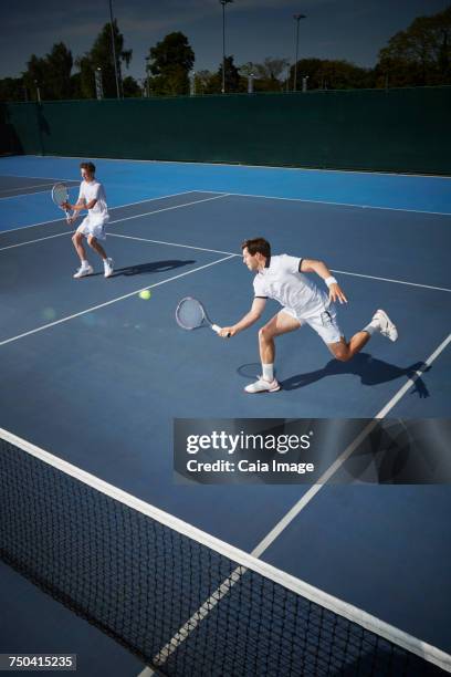 young male tennis doubles players playing tennis, reaching for the ball on sunny blue tennis court - doubles sports competition format stock pictures, royalty-free photos & images