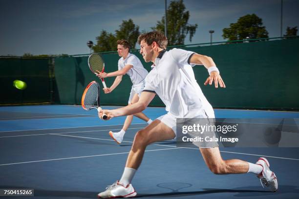 young male tennis doubles players playing tennis, hitting the ball on blue tennis court - tennis player stock pictures, royalty-free photos & images