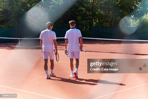 young male tennis players walking with tennis rackets on sunny clay tennis court - tennis player stock pictures, royalty-free photos & images