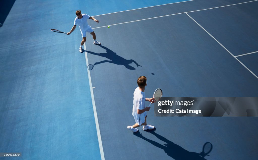 Young male doubles tennis players playing tennis on sunny blue tennis court