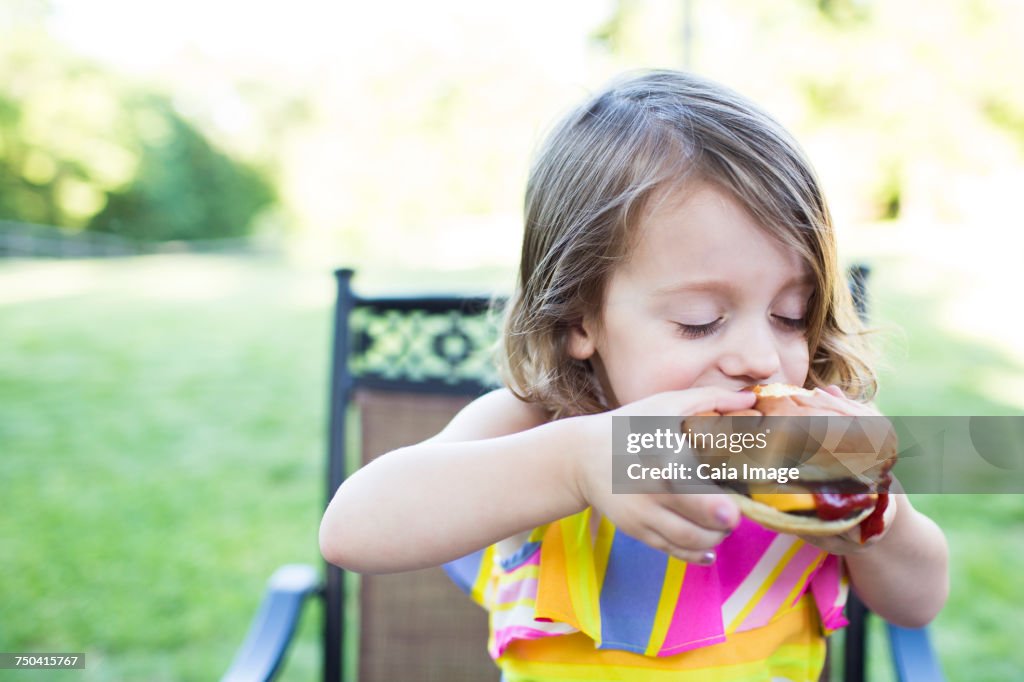 Preschool girl eating messy cheeseburger on patio