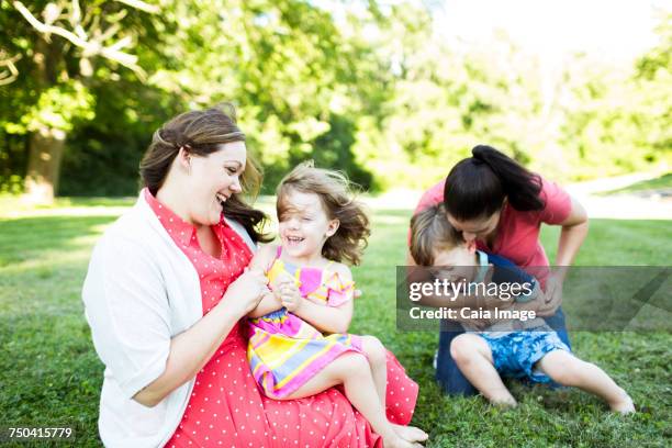 Lesbian mothers playing, tickling children in summer grass yard